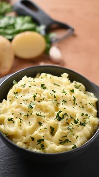 Bowl of creamy mashed potatoes rotating on wooden table