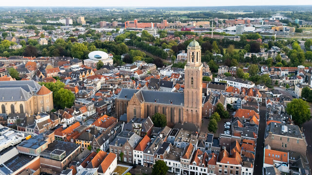 Aerial view of the Grote Kerk in the historic city center of Zwolle, surrounded by dense urban rooftops, narrow streets, and lush green trees in Zwolle, Overijssel, Netherlands.
