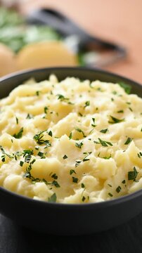 Bowl of creamy mashed potatoes rotating on wooden table