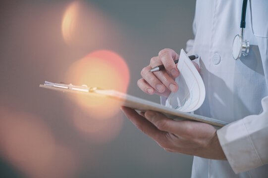 Male doctor wearing white cloth and stethoscope using pen and paper report analysing patient diagnosis data in medicine and healthcare concept