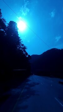 Vertical Mountain Road at Sunset with Bright Sun and Blue Sky  Scenic Himalayan Hill Landscape  Silhouette of Trees and Mountains  Peaceful Road Journey  Travel and Nature Background