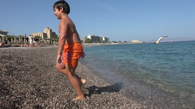 Rhodes Town, Greece - 23 ofOctober 2023: Chubby boy walking out of the sea and falling on the beach
