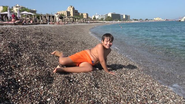Rhodes Town, Greece - 23 ofOctober 2023: Playful chubby boy tumbling and falling on the pebble beach
