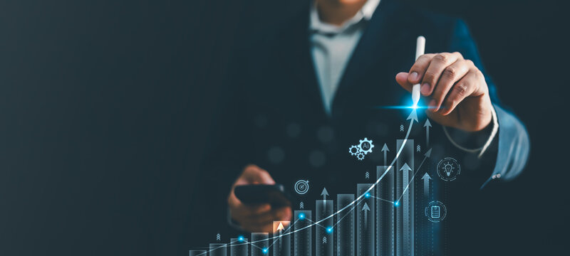 Businessman hand drawing glowing growing financial stock graph with stylus pen. Concept of business growth, investment return, artificial intelligence analytics, target achievement and success