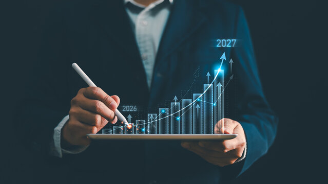 Businessman hand drawing glowing financial stock graph on tablet from year 2026 to 2027. Concept of business growth, investment return, future target forecast, planning strategy and success