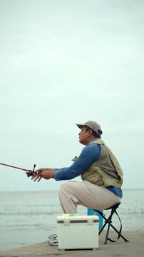 Happy senior man sitting by the sea and fishing with a rod after retirement. Active aging, healthy longevity, outdoor leisure, fulfilling retirement. Life insurance and financial security concept.
