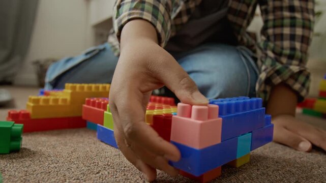 Child playing with colorful plastic building blocks on floor, developing fine motor skills. Ideal for early childhood education marketing and parenting campaigns