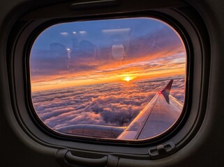 Naklejka premium Airplane window view of sunset above clouds with aircraft wing visible in flight