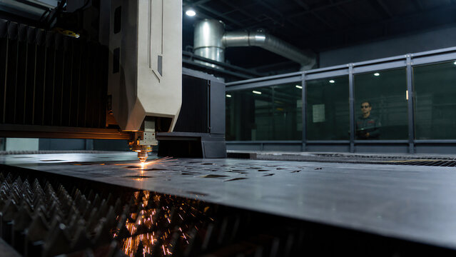 Industrial laser machine cutting steel sheet. Operator watching metalworking process in manufacturing factory. Modern cnc equipment for precision metal fabrication and engineering.