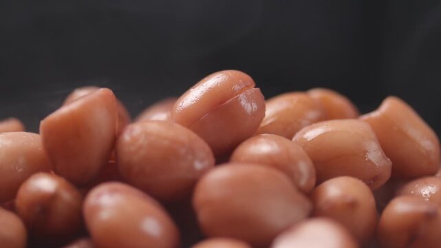 pile of shelled boiled peanuts with steam rising, slowly rotating on a black background.