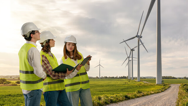 Engineers discussing renewable energy wind farm project using digital tablet. Concept of infrastructure planning, green investment, and clean power consulting.