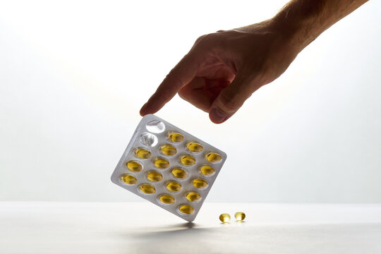 Hand Reaching for Blister Pack of Yellow Vitamin Oil Capsules on White Background