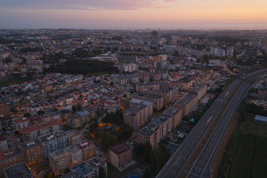 Aerial view of the residential cityscape of Maia at sunset, featuring dense apartment blocks, urban streets, and a highway running alongside the town in Maia, Porto District, Portugal.