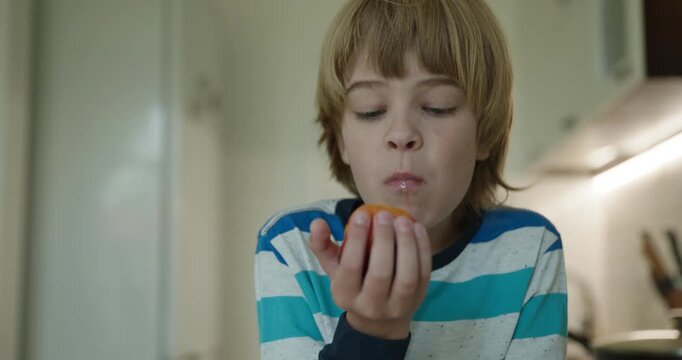 Caucasian kid boy enjoy eating peach in kitchen. 4K 10-bit