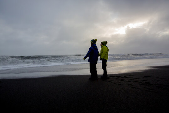 Children running from and to the ocean in black sand beach of Reynisfjara and the mount Reynisfjall in Iceland on a cold rainy day