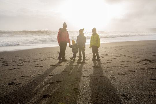 Family posing against the sun in black sand beach of Reynisfjara and the mount Reynisfjall in Iceland