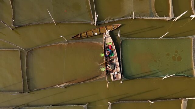 Aerial view of fishermen working in a wooden boat amidst fish farming nets on Lake Rawa Pening in Waduk Rawapening, Central Java, Indonesia.