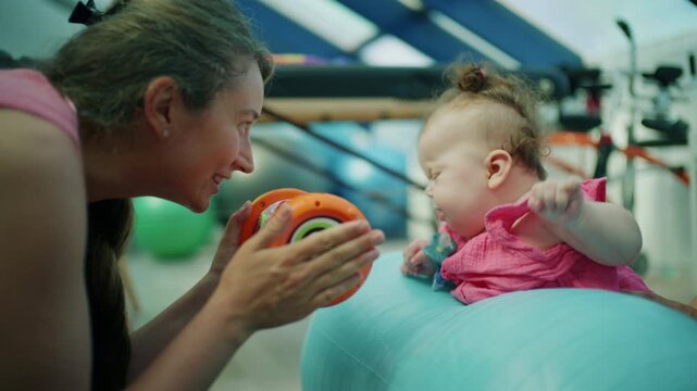 Infant doing motor skill exercises with a therapist using a toy on an exercise ball, promoting early development