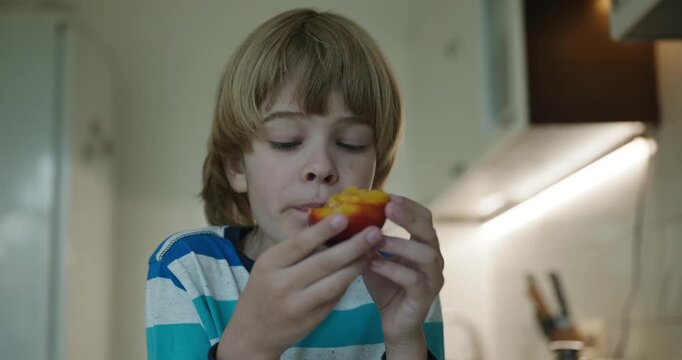 Caucasian kid boy enjoy eating peach in kitchen. 4K 10-bit
