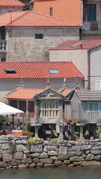 Vertical 9:16 video crop showing iconic stone horreos (traditional granaries) on stone pillars, set along the waterfront in Combarro, Galicia, Spain. No people are visible.