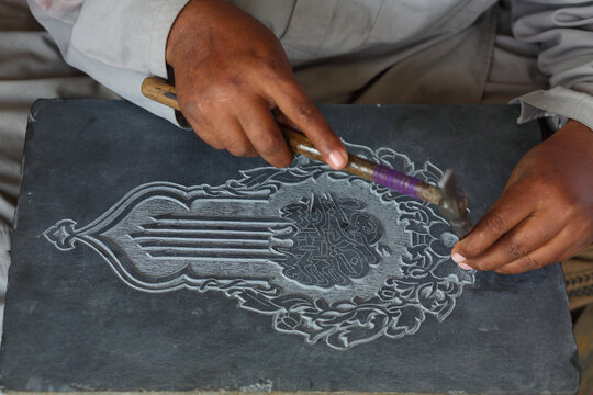 View of a skilled artisan carving intricate calligraphy into a stone slab using a hammer and chisel in Lahore, Punjab, Pakistan.