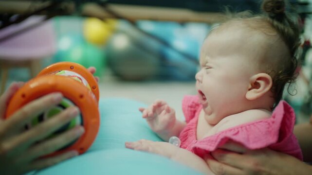 Infant with down syndrome receiving physical therapy, engaging with an educational toy for motor skills development and early intervention care