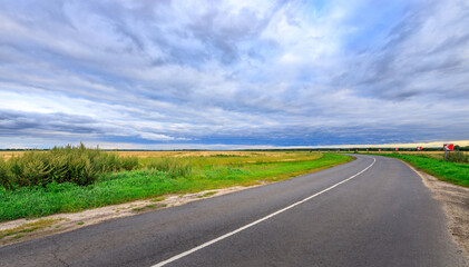 Fototapeta premium Lonely road winds across grassy plains under dramatic cloud cover