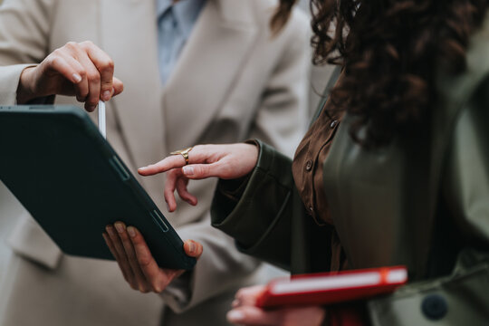 Two colleagues review documents on a tablet while one points with a stylus. The pair consult a smartphone and tablet together in a casual business meeting.