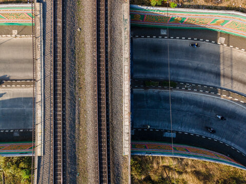 Aerial view of a railway bridge crossing over a road with motorcycles passing underneath in Purwokerto, Central Java, Indonesia.