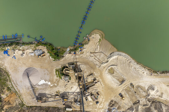 Aerial view of sand and gravel quarry with machinery, conveyor belts, and piles of sand next to a water reservoir in Poland.