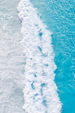 Aerial view of turquoise ocean waves crashing onto the sandy shore with white sea foam in Esperance, Western Australia, Australia.