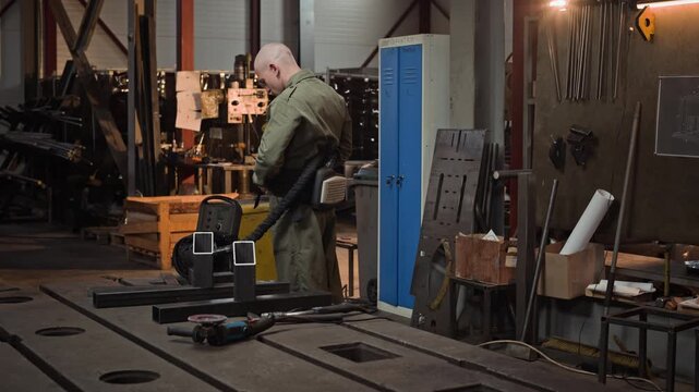 Young adult Caucasian male welder putting on protective welding helmet with air respirator system in industrial workshop. Ideal for manufacturing safety training or industrial workforce videos