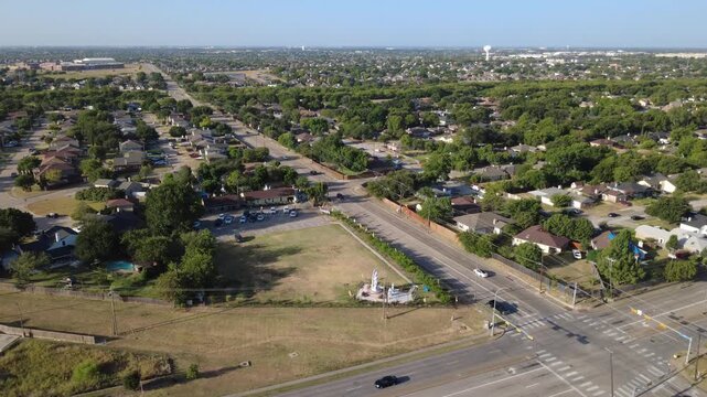 Broad asphalt thoroughfares guide traffic past East Sublett Road shopping center. Grassy open lots transition into leafy single family residential tracts, green foliage, Arlington, Texas