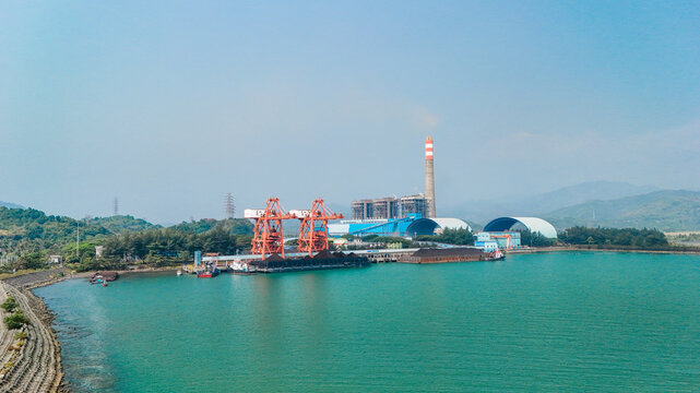 Aerial view of a coal-fired power plant facility with large orange cranes loading barges, symbolizing electricity supply, industry and environmental pressure