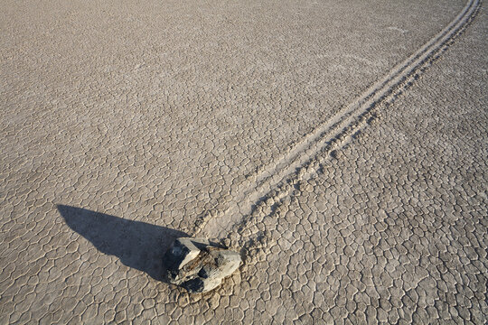 View of a sailing stone leaving a long trail on the cracked, dry mud surface of Racetrack Playa in Death Valley, California, United States.