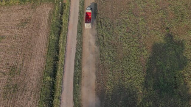 Aerial drone view of a green tractor towing a trailer across agricultural land in Lombardy, Italy, traveling toward the corn harvest during the farming season.