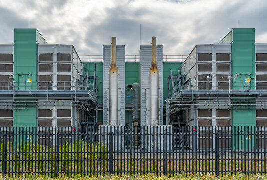 View of the modern data center facility featuring industrial cooling towers, metal ventilation units, and a secure perimeter fence in Middenmeer, North Holland, Netherlands.