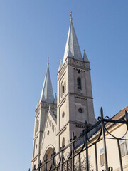 Fototapeta premium Church with twin spires against a clear blue sky, ornate stone facade, arched entrance, and a wrought iron fence in the foreground, highlighting Gothic influence