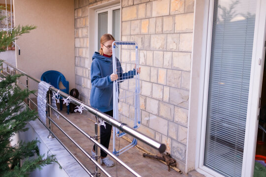 Teenage girl putting away a drying rack on a balcony with a cocker spaniel.