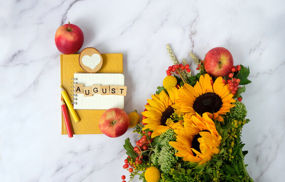 autumnal bouquet with sunflowers, notepad, pencils, book and red apples on marble table background. august month calendar concept. summer end seasonal composition. flat lay