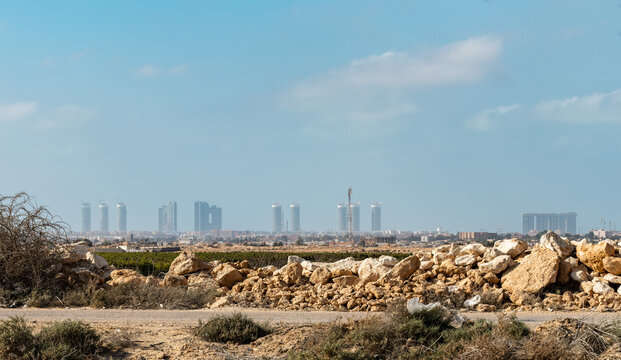 View of the modern skyline of New Alamein City rising above the arid landscape with rocky foreground and sparse desert vegetation in Al Alameen City, Marsa Matrouh Governo, Egypt.
