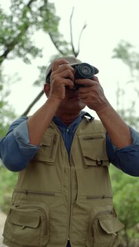 Happy senior man walking through a forest while taking photos of nature. Active aging, retirement lifestyle creative hobby, healthy longevity. Life insurance and fulfilling life after retirement.
