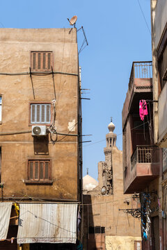 View of the Mosque and Khanqah of Al-Nasir Faraj Ibn Barquq framed by traditional buildings with wooden shutters and balconies in El-Gamaleya, Cairo Governorate, Egypt.