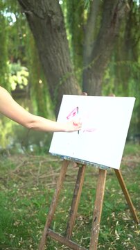 Beautiful woman artist painting on a canvas by the river in a dress
