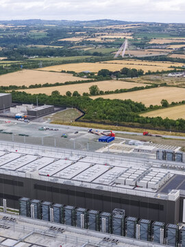 Aerial view of a large industrial data center facility with extensive rooftop cooling units, set against rural fields and the Mary McAleese Boyne Valley Bridge in Drogheda, County Louth, Ireland.