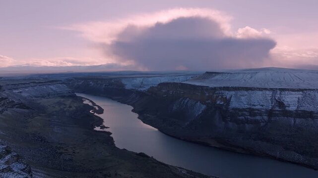 Aerial view of the snow-dusted Snake River canyon within the Morley Nelson Snake River Birds of Prey National Conservation Area under a soft sunset sky in Murphy, Idaho, United States.