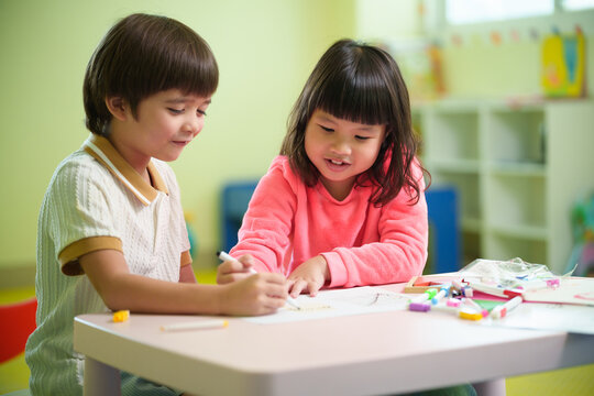 Two preschool children enjoy drawing together in a colorful classroom, encouraging creativity, teamwork, and early learning through hands-on art activities.