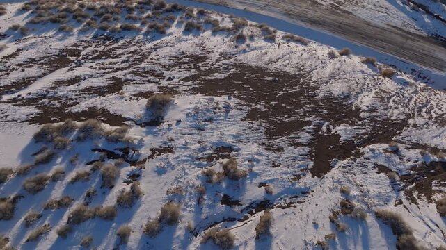 Aerial view of the snow-covered landscape of the Morley Nelson Snake River Birds of Prey National Conservation Area with scattered shrubs and long shadows in Murphy, Idaho, United States.