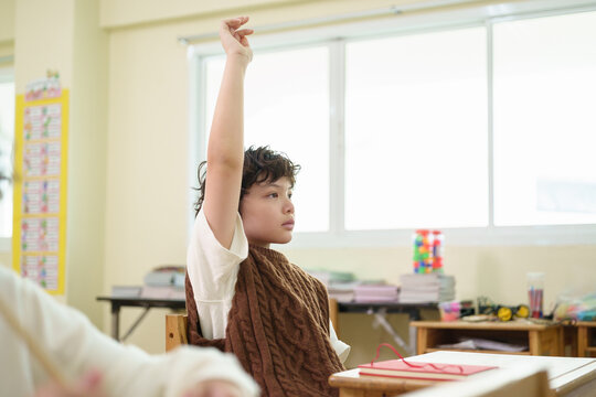 Young student raises a hand to answer a classroom question, showing confidence, participation, and active learning in an engaging school lesson.