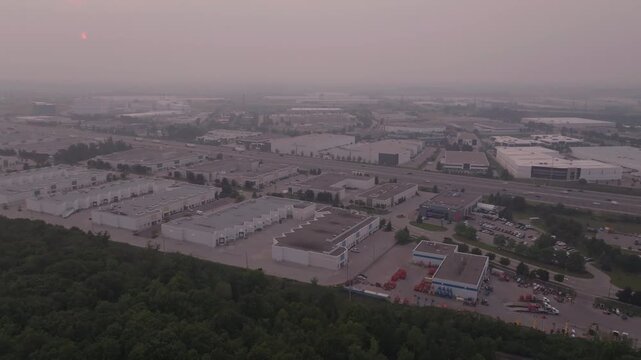 A high angle drone view reveals industrial zones near Highway 401 obscured by thick wildfire smoke. The hazy atmosphere reduces visibility across warehouses and empty parking lots.